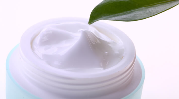 Photo showing white moisturizing cream with a green leaf above.