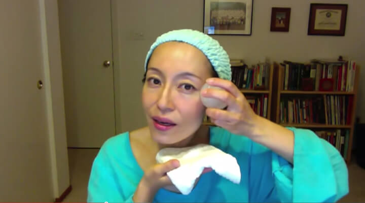 Fumiko Takatsu holding an ice ball on her temple while showing how to reduce under eye bags.