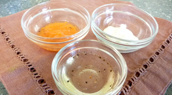 Three small glass bowls, the first one filled with shredded carrots, the second one with oil and the third one with white powder.