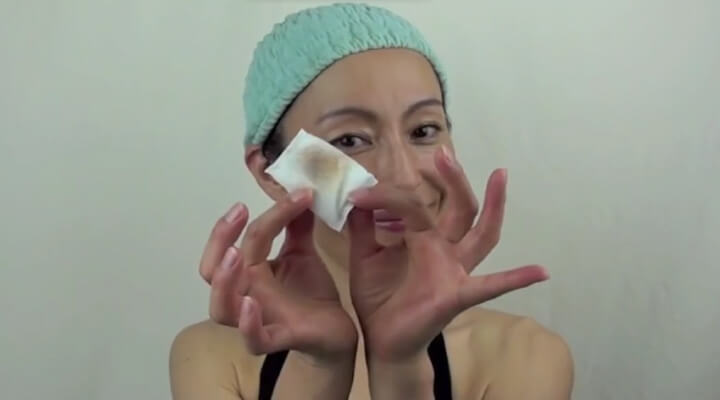 A woman with a green shower cap holding a white pad for makeup removing and smiling