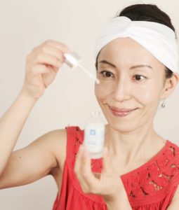 Fumiko Takatsu with a white head band smiling while opening a bottle of face cream. 