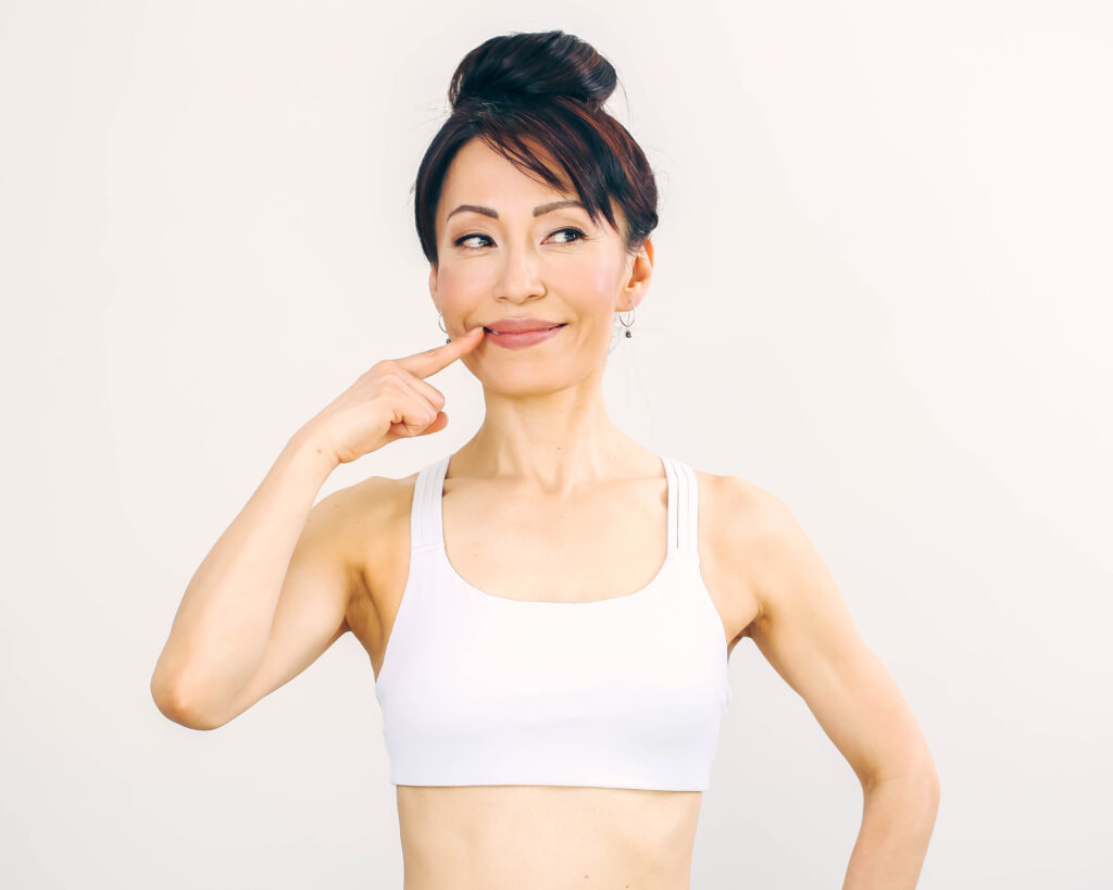 Fumiko Takatsu in a white sports bra smiling while pointing at her lips.