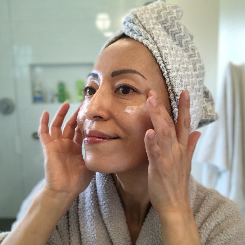 Fumiko Takatsu looking at the mirror while applying white face cream on her cheeks.