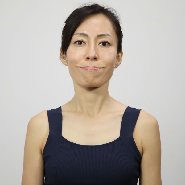 Woman in black tank top doing face yoga exercise for more symmetrical mouth