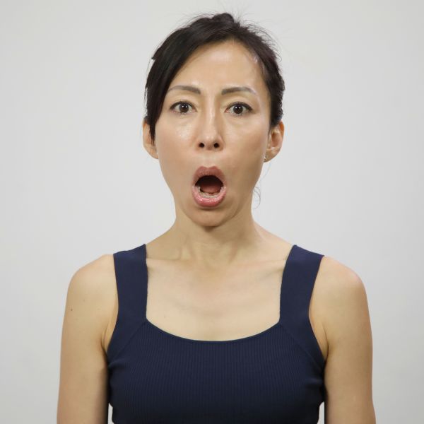 Woman in black tank top doing face yoga exercise for more symmetrical face