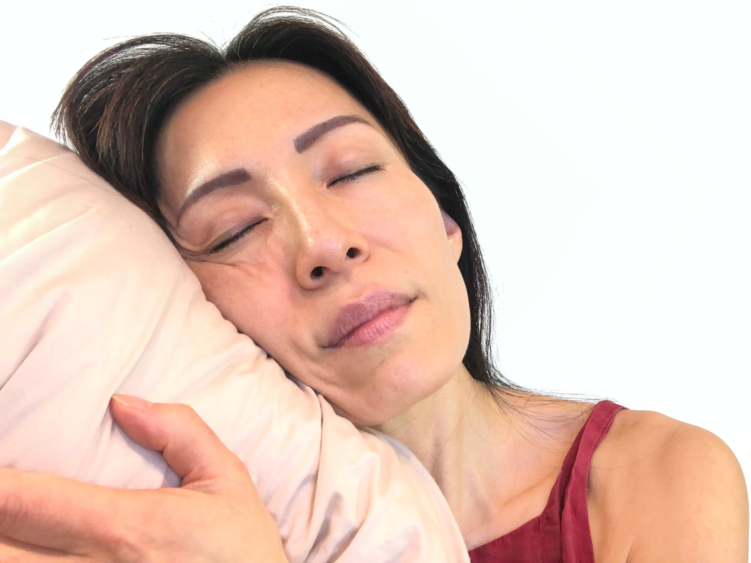 A woman is sleeping on her side, pressing her face against the pillow, causing lines and wrinkles to form.